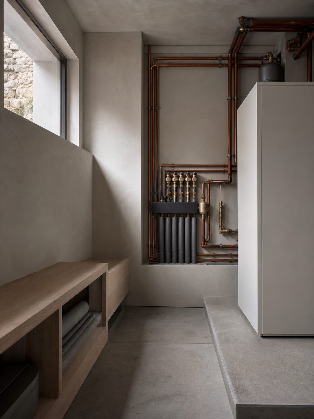 A well-ordered plant room with copper pipework and labelled valves, lit by a high window.