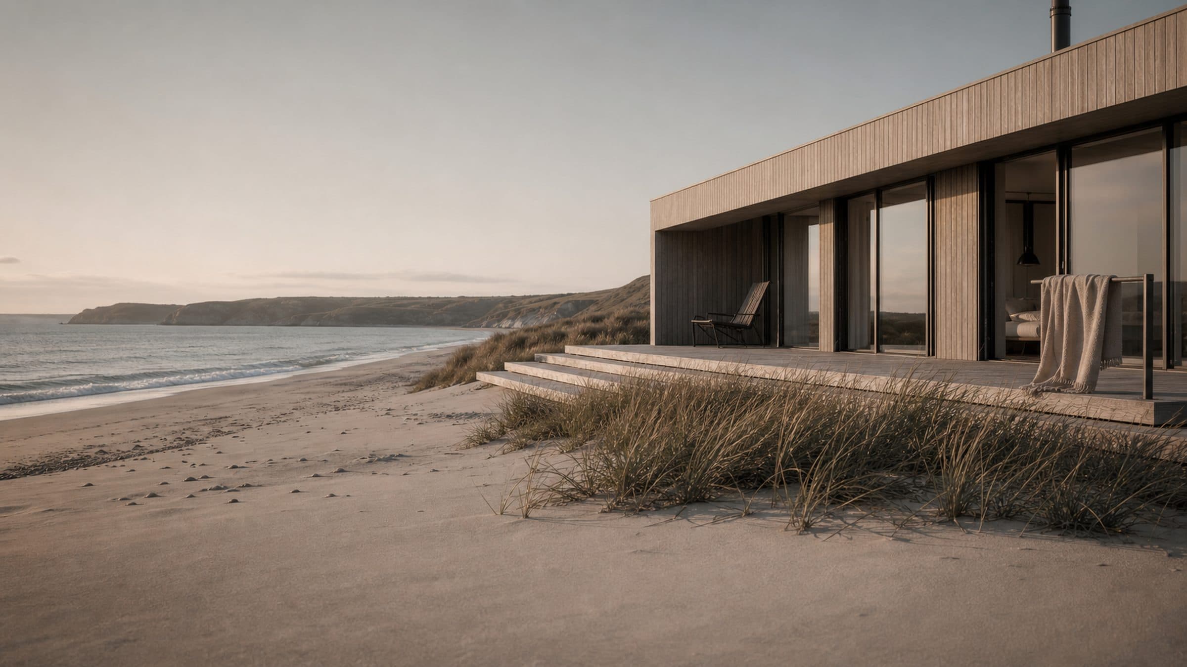 A timber terrace at beach level with open doors and low evening light across the sand.