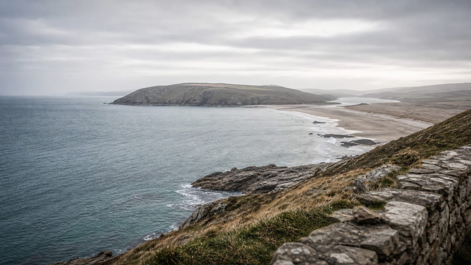 A wide view of a coastline in flat winter light, headland and estuary receding into haze.