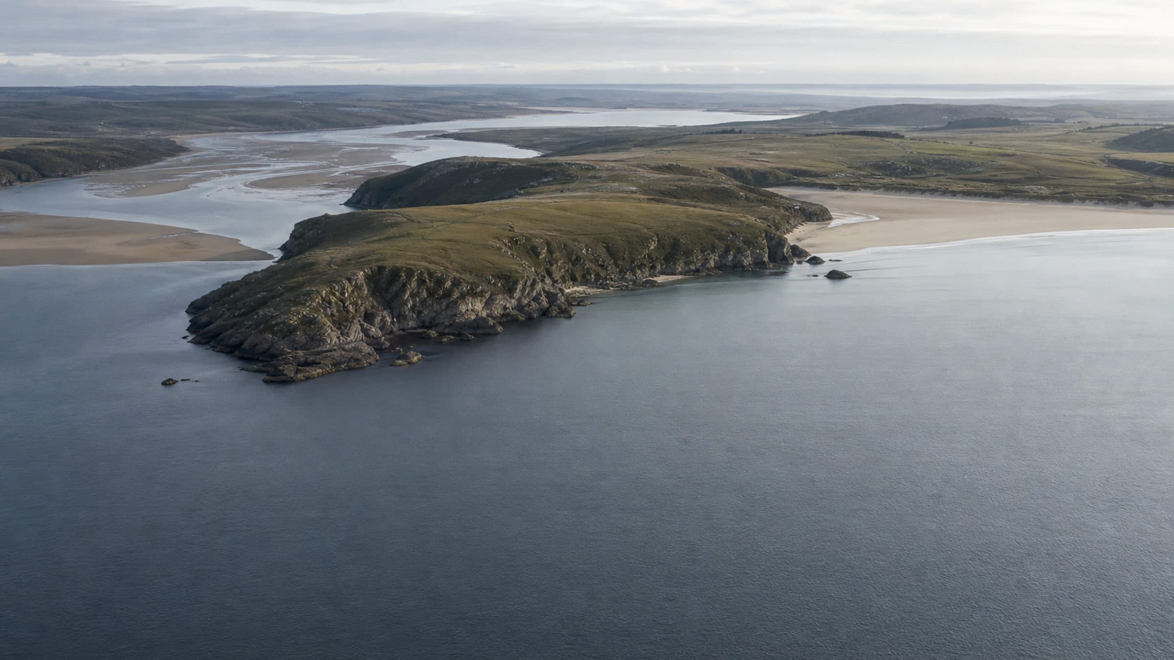 The Vellan Coast seen from the air in flat morning light, headland, bay and estuary in one frame.