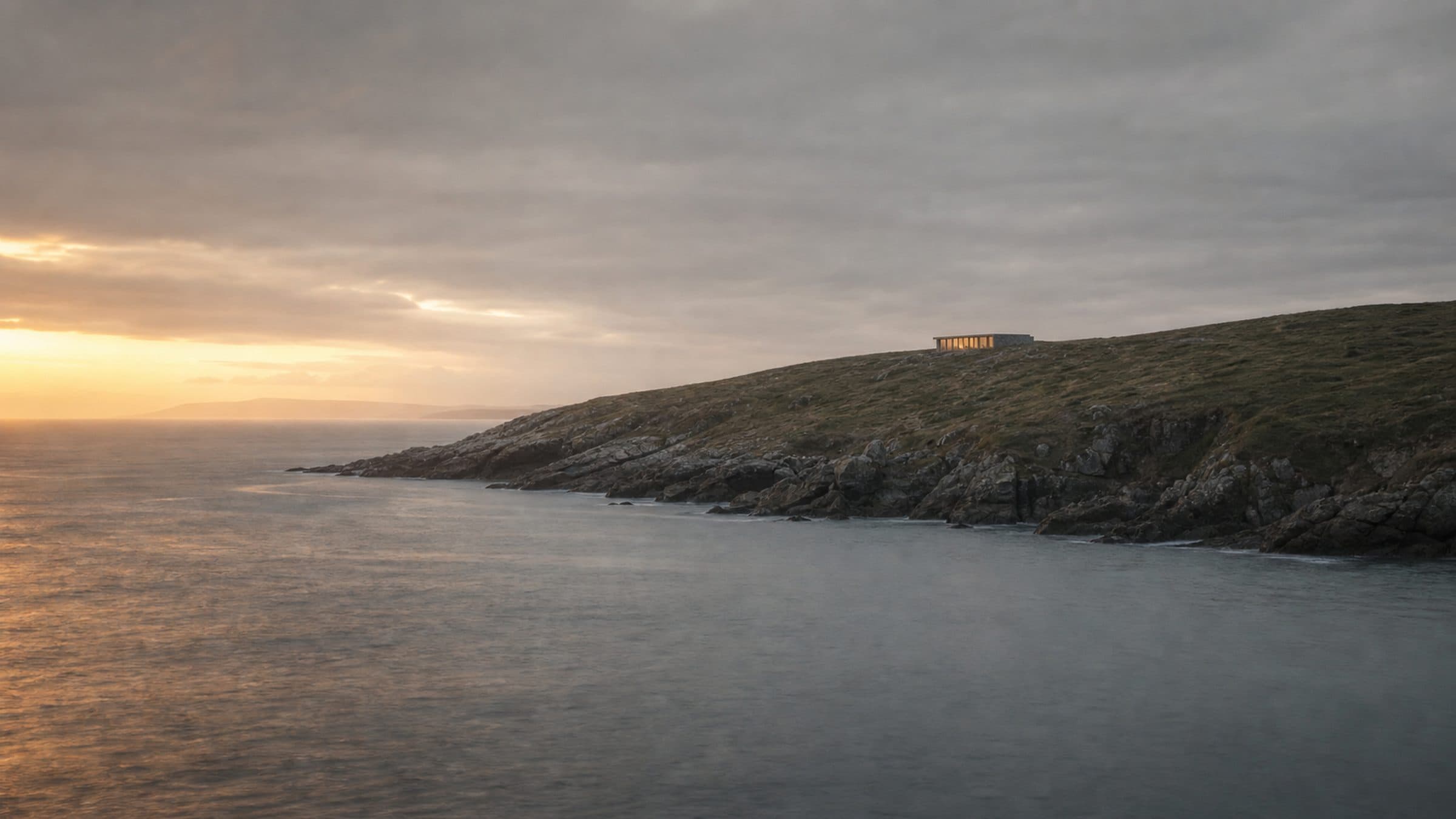 A stretch of coastline in evening light with a low modern house on the headland above it.
