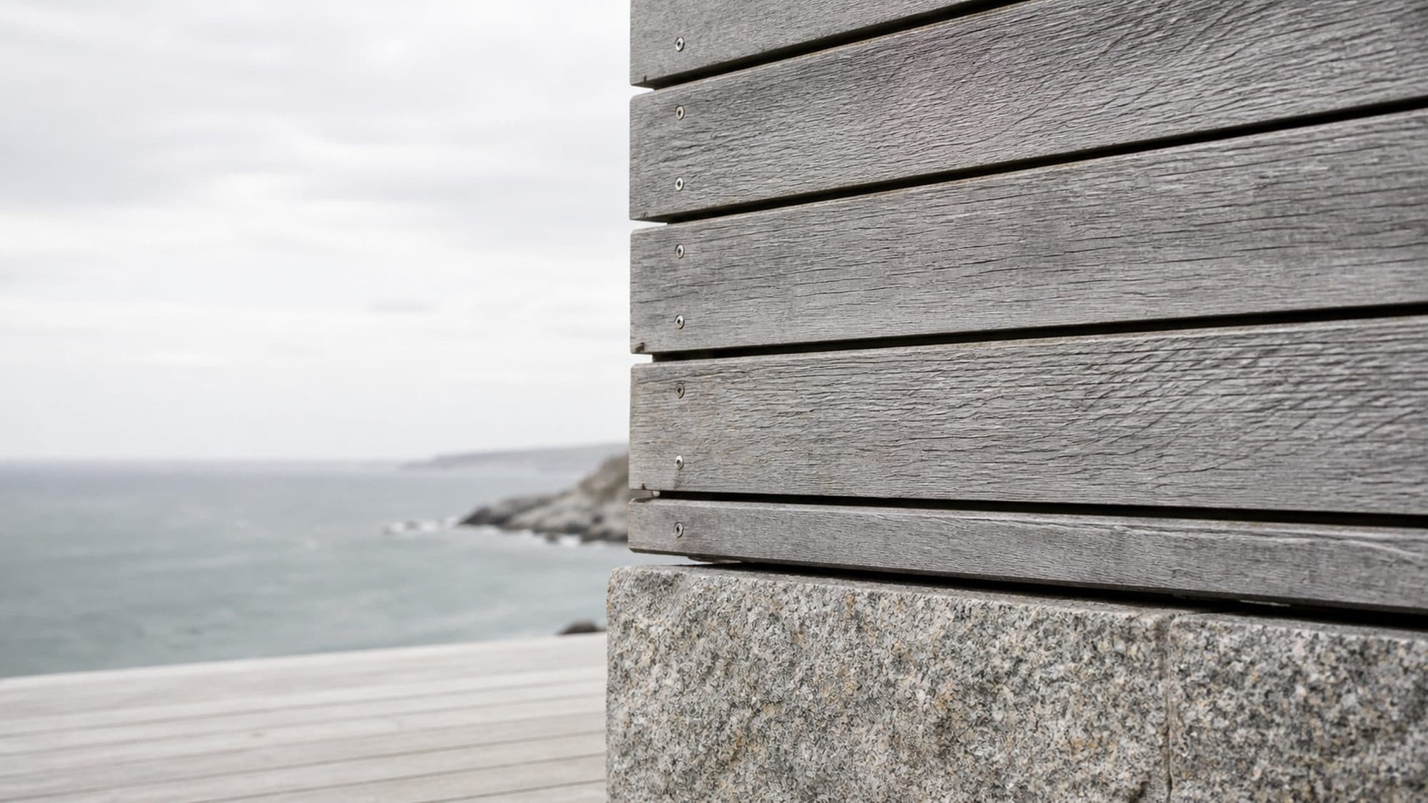 Salt-weathered oak and granite detailing on a coastal house, photographed in flat overcast light.