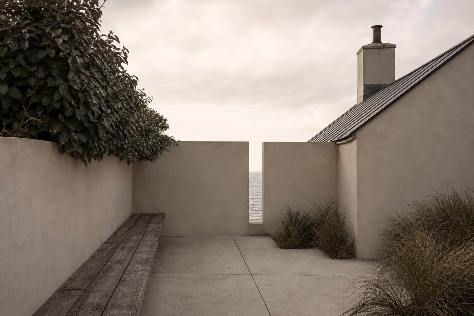 A sheltered courtyard with lime-rendered walls, an oak bench and a narrow framed strip of sea beyond.
